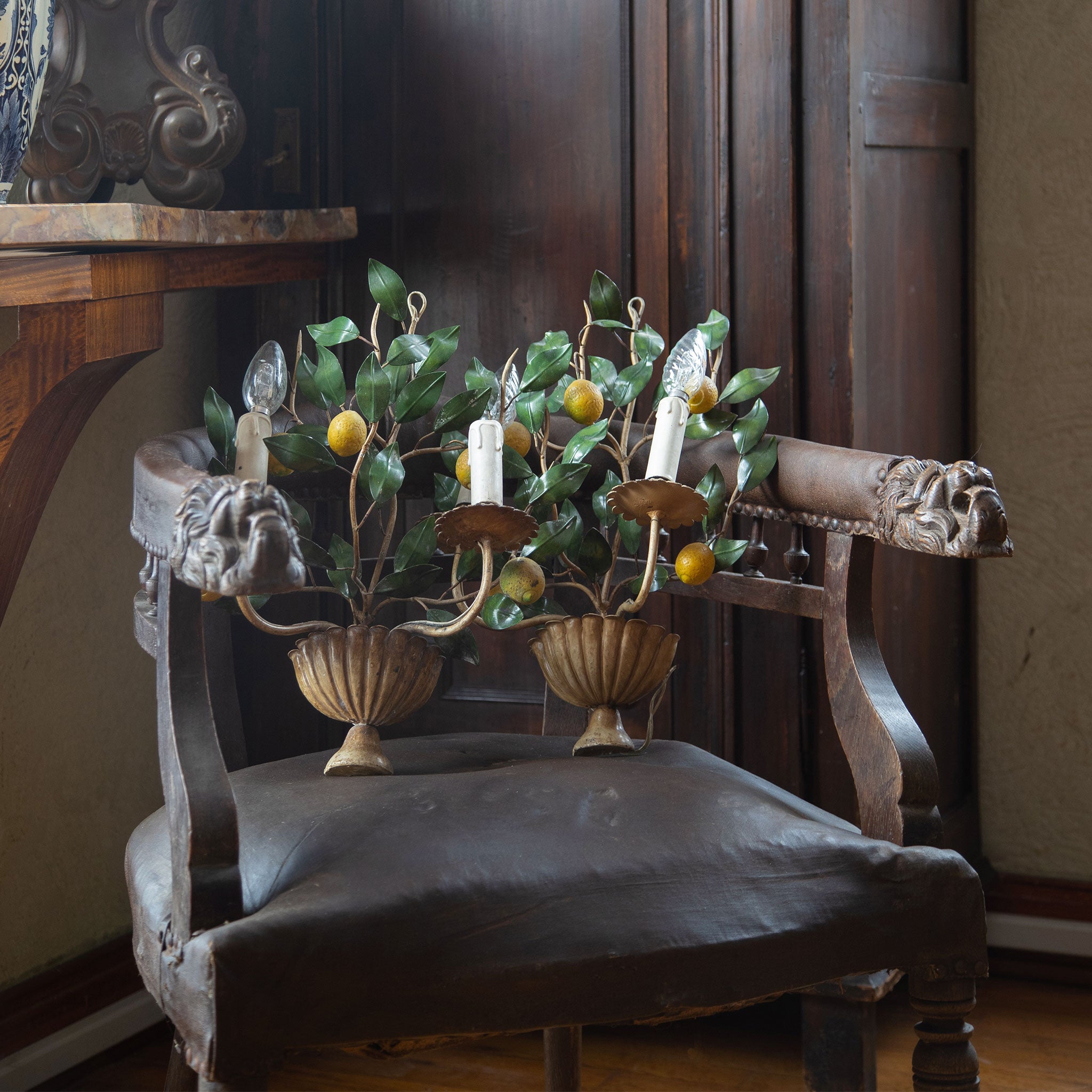An antique leather covered carved english side chair with two vintage metal tole lemon sconces sitting atop it. 