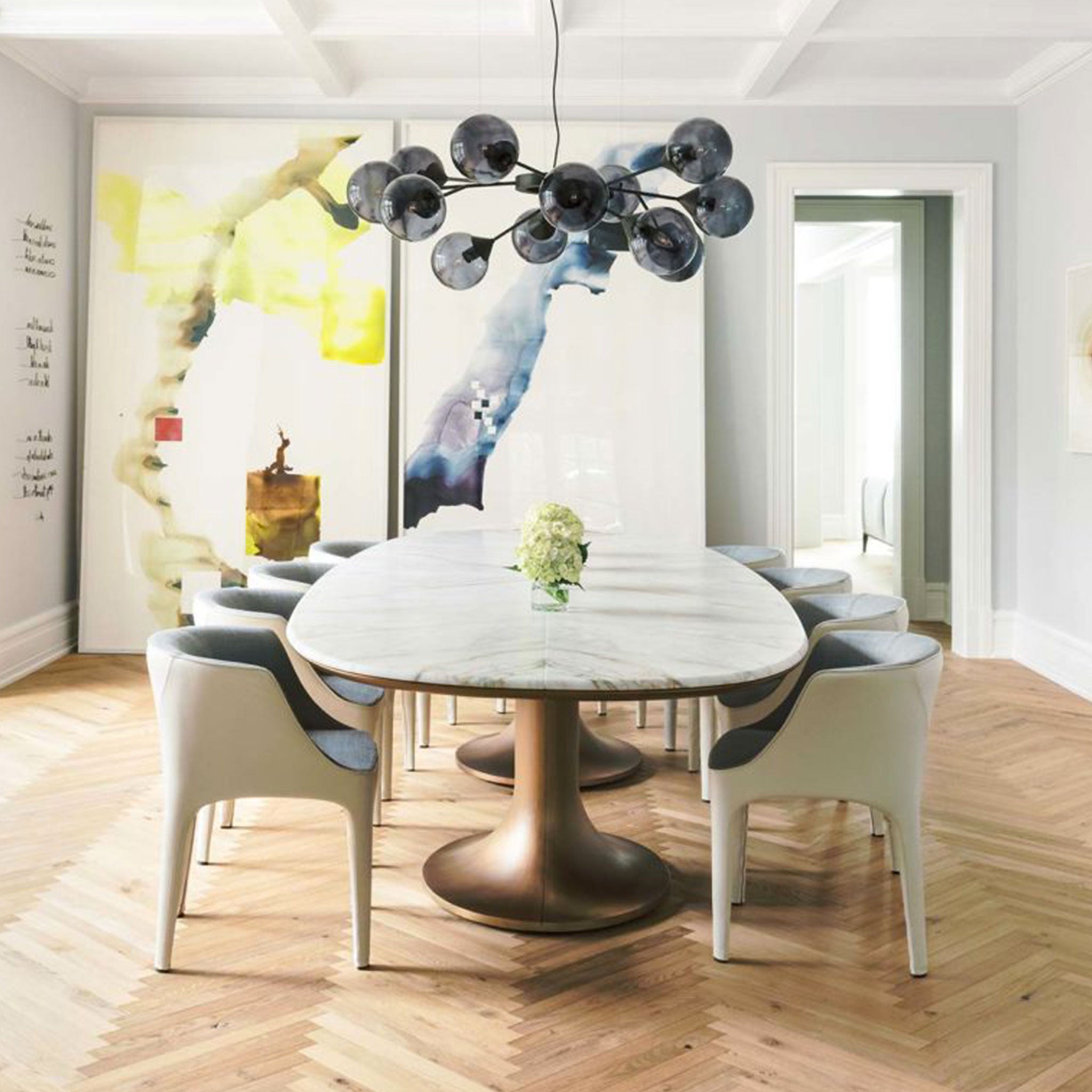 A modern dining room with chevron wood floors, a marble dining table with contemporary upholstered chairs and a smoky glass chandelier.