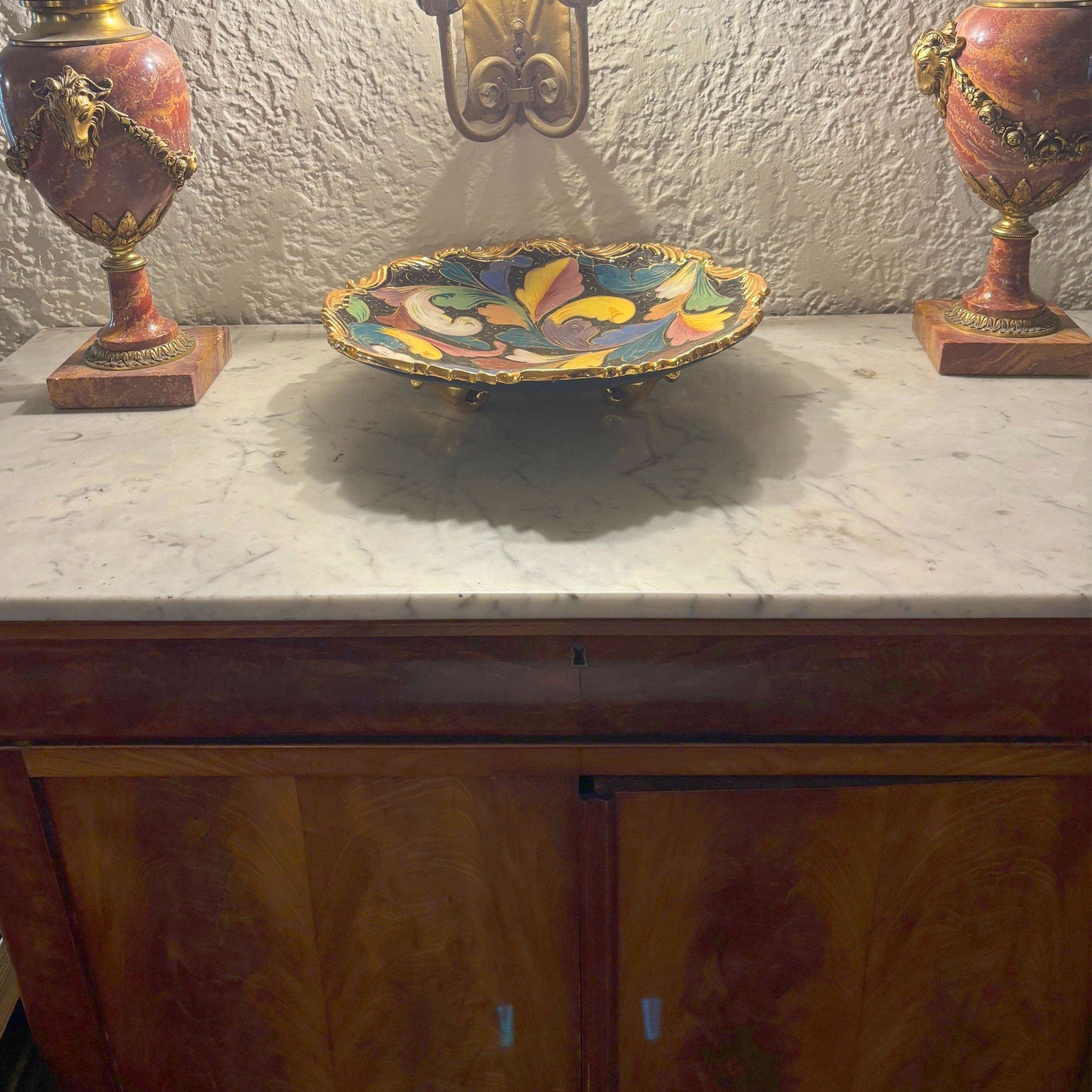 Decorative bowl with floral design on a marble surface, flanked by two ornate lamps.